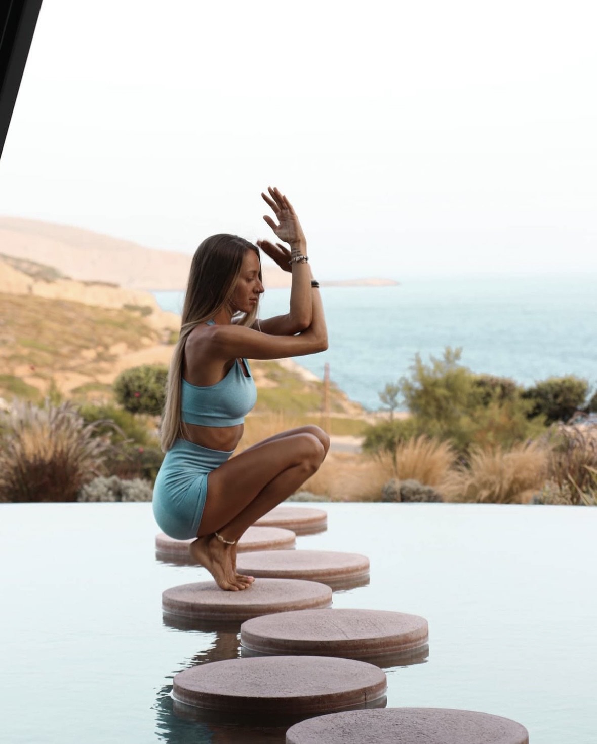 Stefania, an Omreset instructor is in Malasana pose on stones in the water.